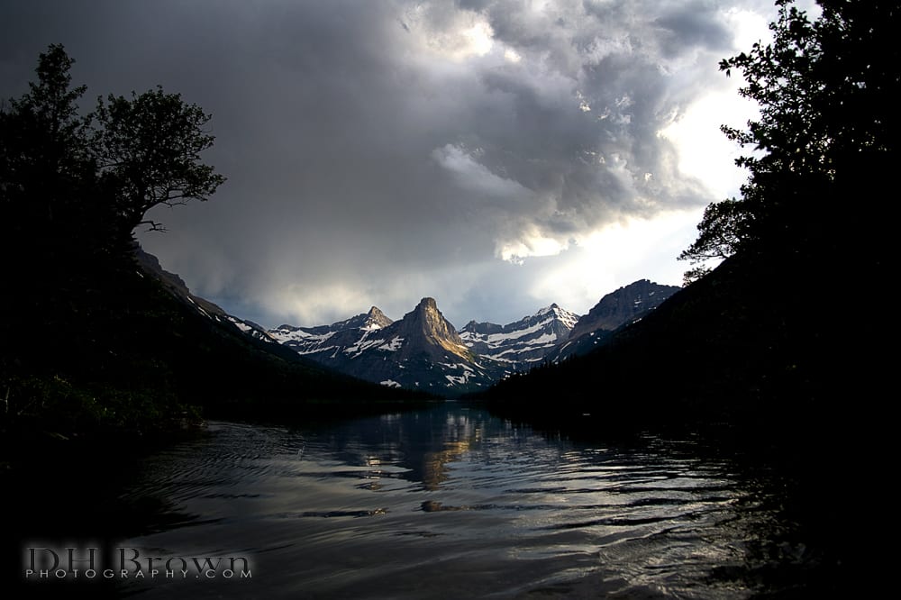 Pyramid Peak with a passing storm is reflected in the outflow of Glenns Lake, Glacier National Park.